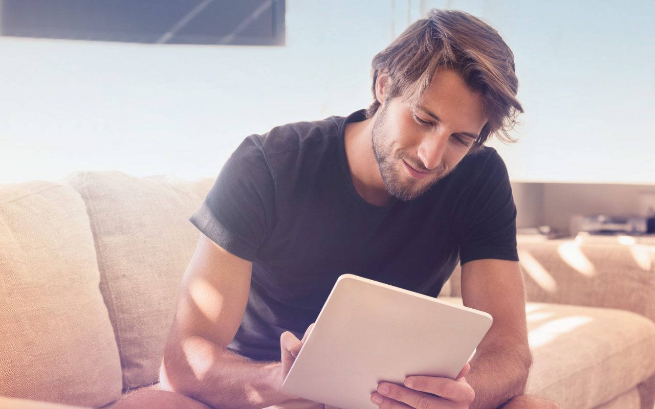 Arvato Systems_Commerce_Man on couch looking on tablet smiling